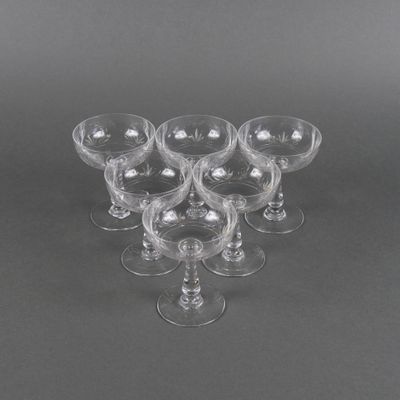 six verres à vin transparents sont disposés en triangle sur une surface grise