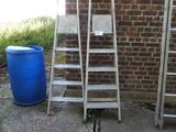 a ladder leaning against a brick wall next to a blue barrel