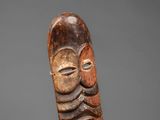 a carved wooden mask with a face on a gray background
