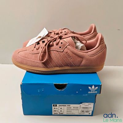 des baskets Adidas roses posées sur une boîte bleue, sur une surface blanche
