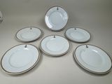 six assiettes blanches à bord doré sont disposées sur une table