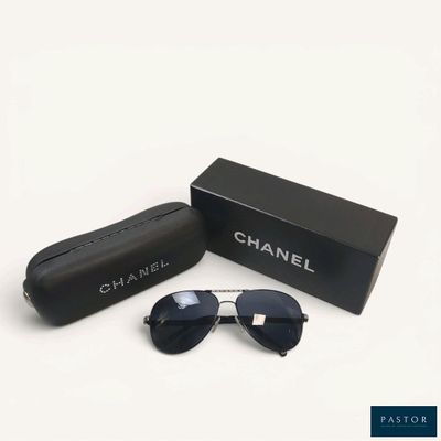 Des lunettes de soleil Chanel dans un coffret noir et un étui, posés sur une surface blanche