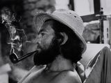 photographie en noir et blanc d'un homme coiffé d'un chapeau et fumant la pipe