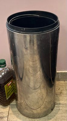 une poubelle en métal posée par terre à côté d'une bouteille de sirop
