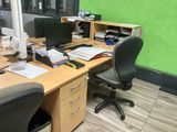 a desk with two computers and a chair in front of a green wall