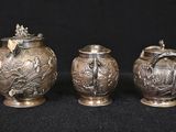 three silver vases sitting on top of a black surface