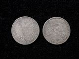 two silver coins on a black surface with a black background