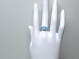 une main blanche à laquelle est passée une bague ornée de trois fleurs bleues