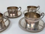 four silver plated cups and saucers on a white surface