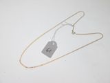 a silver necklace with a tag on it sitting on a white surface