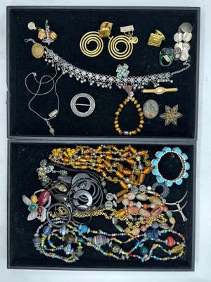 deux boîtes noires remplies de bijoux variés, posées sur une surface blanche