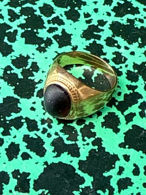 a gold ring with a black stone in it on a green surface
