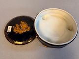 a white bowl with a black lid and a gold emblem on it