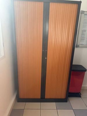 a cabinet in the corner of a room with a red trash can