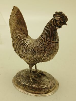 une statue représentant un coq, posée sur un socle, sur une surface blanche