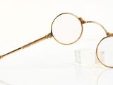 pair of gold - plated eyeglasses on clear surface with reflection