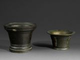 une paire de vases en bronze posés sur une surface grise, sur fond gris