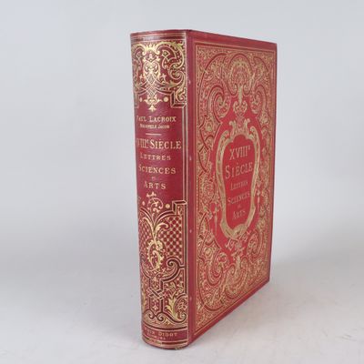 un vieux livre rouge avec des bordures dorées posé sur une surface blanche