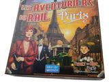 un jeu de société intitulé « Les Aventuriers du Rail : Paris », sur lequel figure l'image d'une femme en robe rouge et d'un homme en smoking
