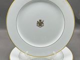 une assiette blanche bordée d'or et ornée d'un emblème doré