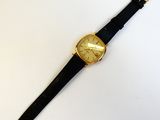 une image représentant une montre en or avec un bracelet noir posée sur une surface blanche