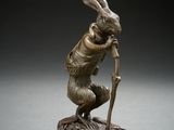 a bronze statue of a rabbit holding a stick on top of a wooden base