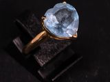 a gold ring with a blue topaz stone on a black surface
