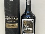 une bouteille de « Red Devil Guyana » avec son coffret, posée sur une table devant un mur blanc