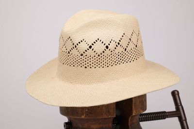un chapeau de paille beige posé sur une chaise en bois dotée d'un accoudoir en bois