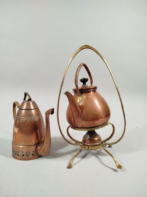 a small copper tea pot and a tea kettle on a stand