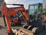 une pelleteuse orange et noire posée au milieu d'un champ de terre