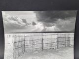 black and white photograph of a fence on a beach with a cloudy sky