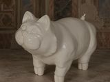 une statue de cochon blanc posée par terre devant un mur