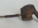 une vieille pipe posée sur une table blanche, à côté d'un bâton en bois