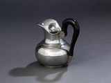 une cruche en argent avec une anse noire posée sur une table