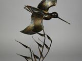 sculpture en bronze représentant un oiseau volant au-dessus des roseaux, posée sur un socle en bois