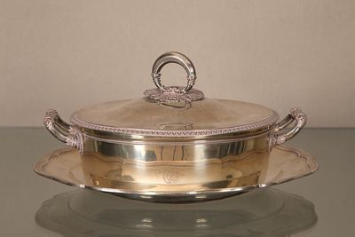 un plateau en argent muni d'un couvercle en argent, posé sur une table en verre
