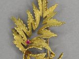 an image of a gold brooch with leaves and a ruby stone
