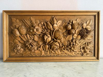 des sculptures représentant des fruits et des fleurs, gravées dans un cadre en bois posé sur une table