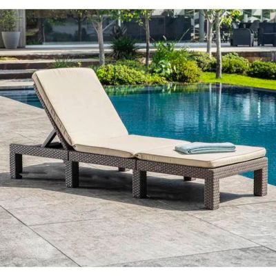 the outdoor chaise lounger is made of wicker and has a beige cushion