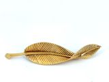 a close up of a gold leaf brooch on a white background