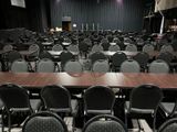rows of chairs and tables in a large room with a projector screen in the background