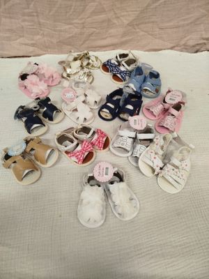 Plusieurs paires de chaussures de bébé sont posées sur un lit recouvert d'une couverture blanche.
