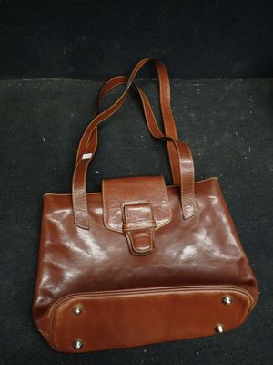 sac à main en cuir marron avec une lanière et des boucles sur un fond noir