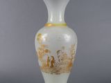 a white vase with gold decoration on it on a gray surface