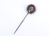 une image représentant une broche en argent sur laquelle est posée une pièce de monnaie, sur un fond blanc