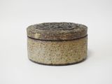une petite boîte ronde avec un couvercle, posée sur une surface blanche