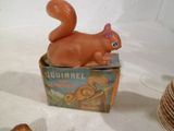 un écureuil en peluche posé sur une boîte, à côté d'une pile d'assiettes