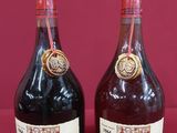 two bottles of wine sitting next to each other on a red surface