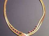 a close up of a gold necklace with pink stones on it